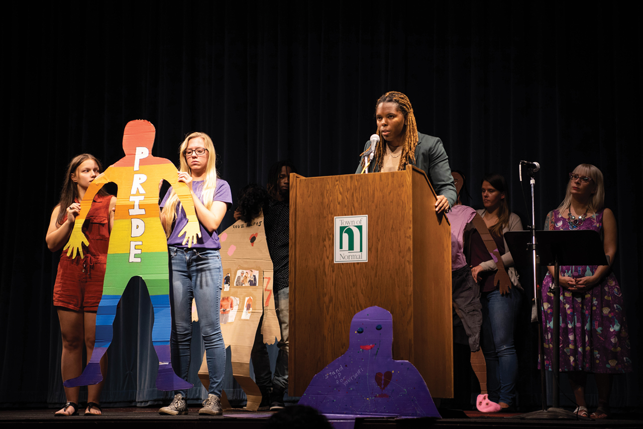 Students holding a cardboard cutout on stage, discussing domestic violence.