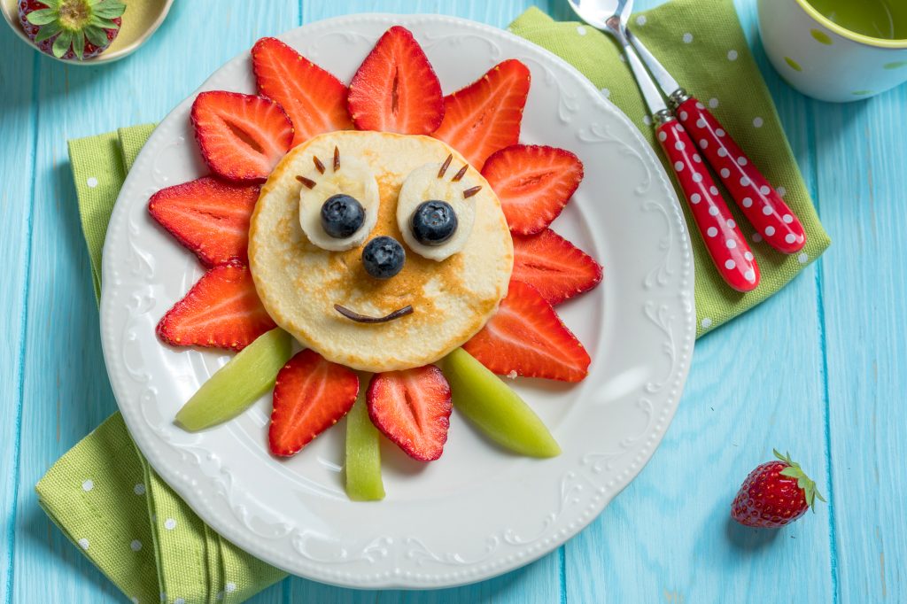 pancake shape dinto a sunflower with straberries for leaves and blueberries for a face