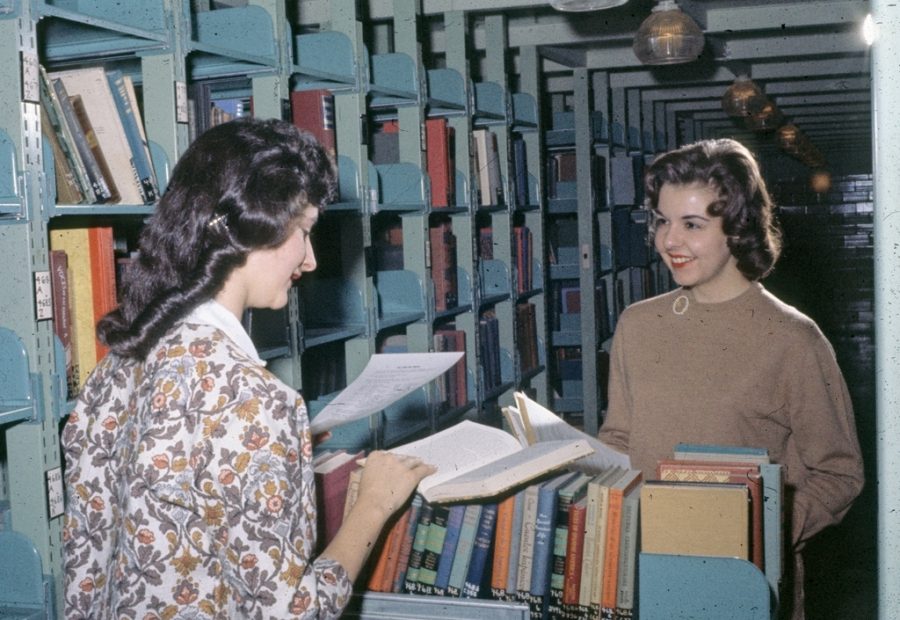 Two women compare books over a book cart in the stacks at Milner Library in 1962