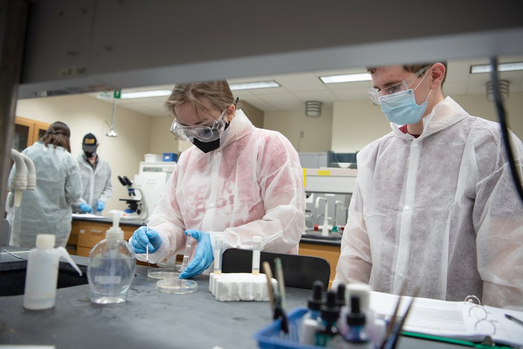 Students in lab coats look at a petri dish in a science lab
