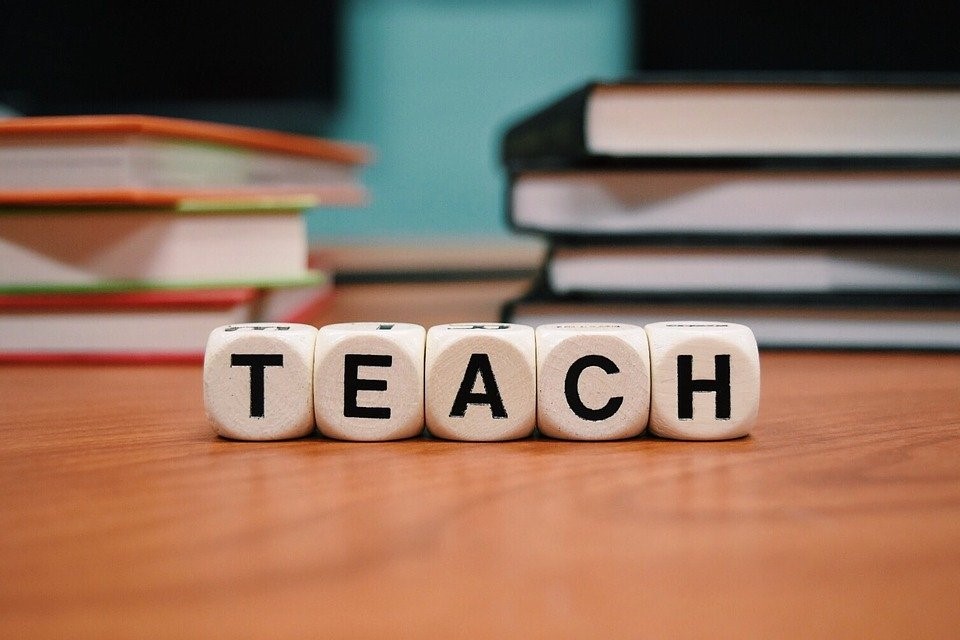 The word TEACH displayed with die on a table