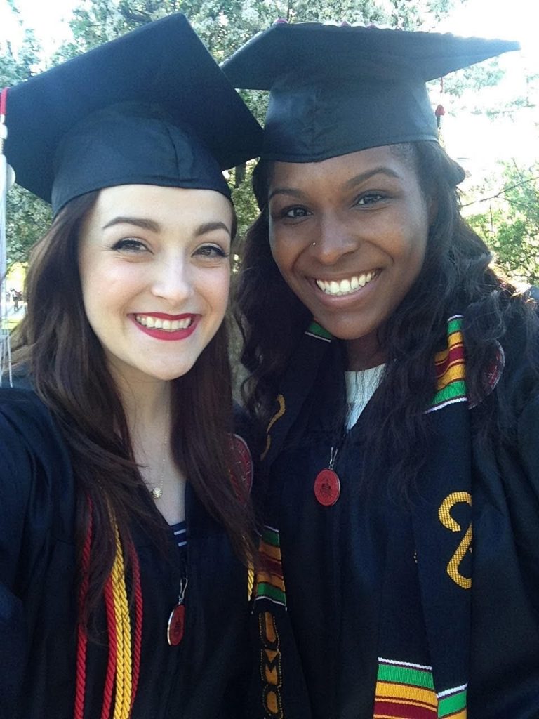 Two women smiling in graduation regalia.