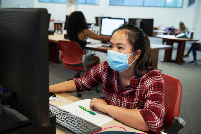 Student wearing a mask using a computer on Milner Library's second floor