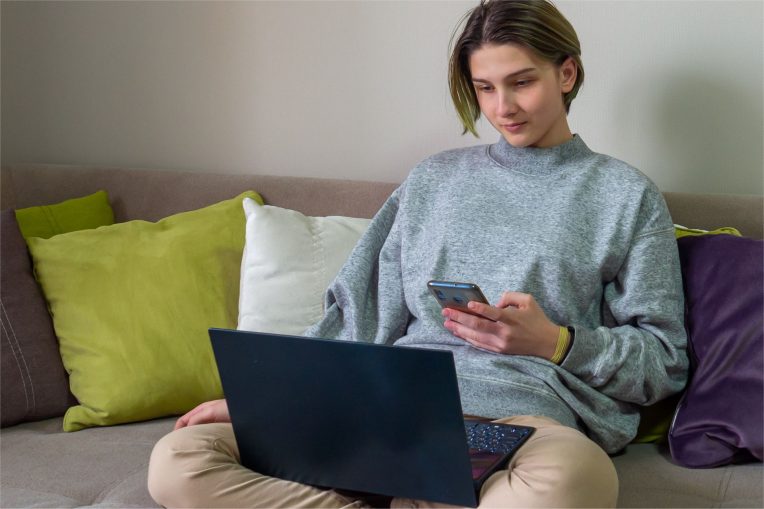 Student on couch with laptop and smartphone