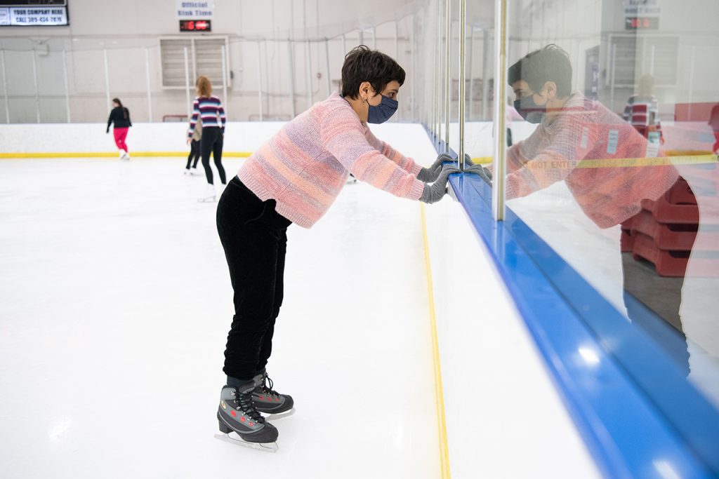 Woman on skates looking through plexiglass at hockey rink. 