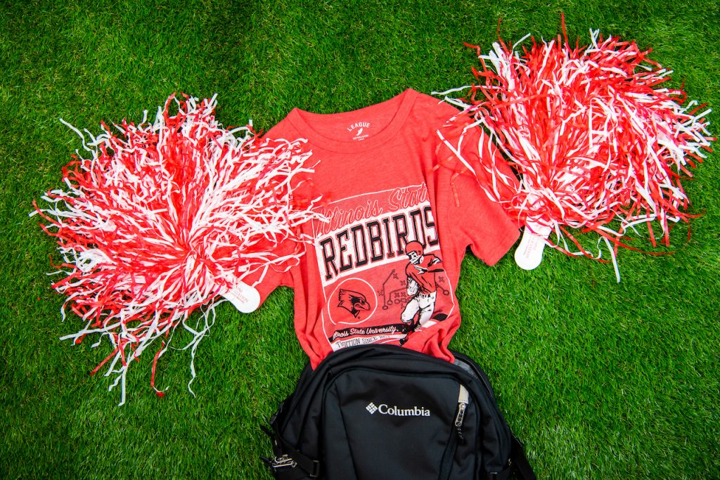Red Redbird t-shirt with a football player on it coming out of a backpack with pom poms by each sleeve as if it were cheering