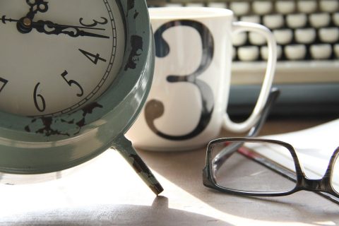 Clock next to a coffee mug with No. 3, glasses, and a keyboard