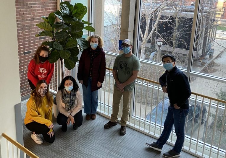 Students and faculty member in middle of stairwell by a plant.