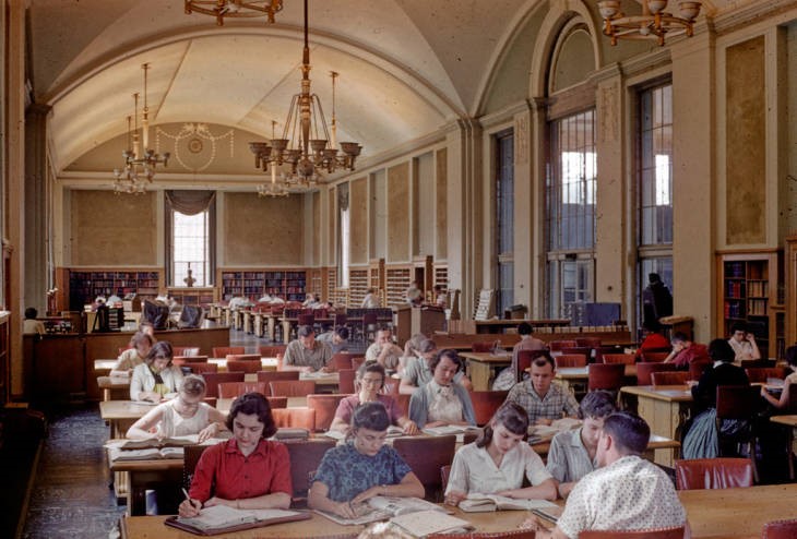 Students studying in the library's Reading Room from June 1959. Students sitting at rows of tables with an ornate ceiling and light fixtures.