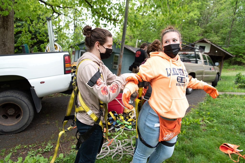 Sophomore philosophy major William Restis (left) helps senior sociology major Anna Raymond adjust her safety harness before heading up onto the roof for the first day of roofing a house.