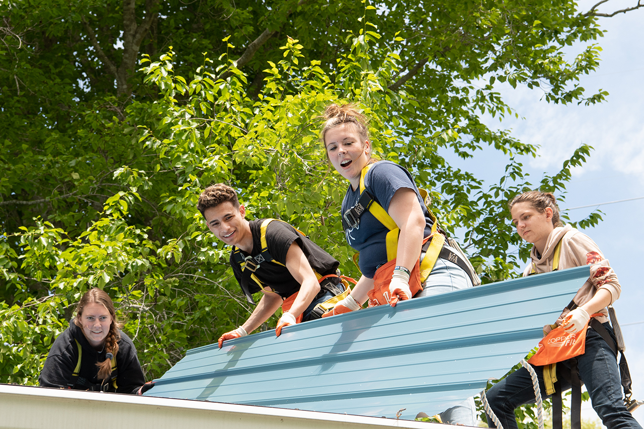 Anna Raymond and Victor Ventura set a new piece of tin roofing material into place on the roof as Nowack, far left, and Restis, far right, look on.