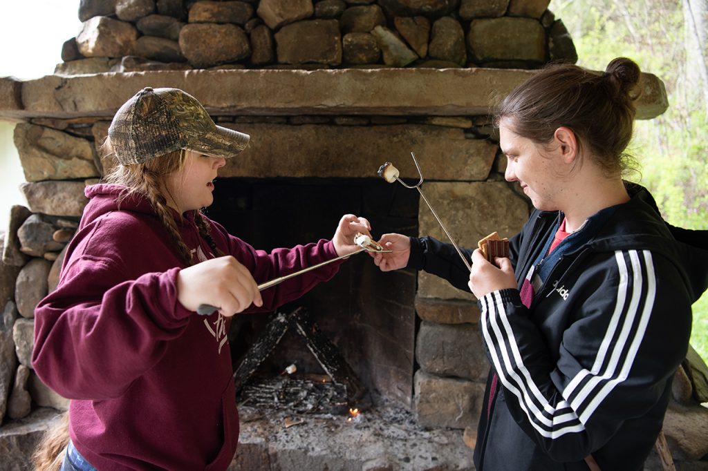 William Restis helps Anna Raymond remove her cooked marshmallow from the campfire stick to make s’mores for a late afternoon snack.