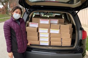 a student stands near the back of a car, packed with boxes of food for donation
