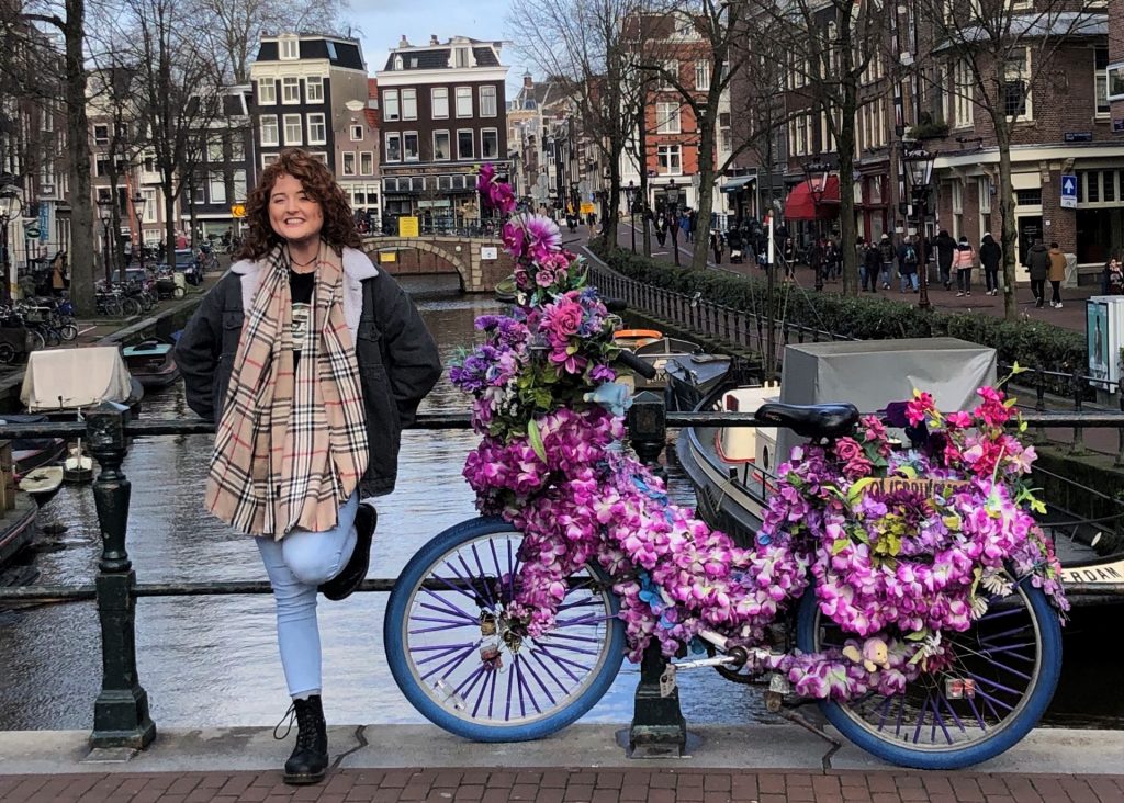 Study abroad student standing next to a bicycle covered in flowers on a bridge in Amsterdam.