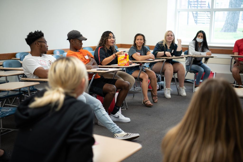 Woman seated in center of a room leads a conversation of first-year students. 