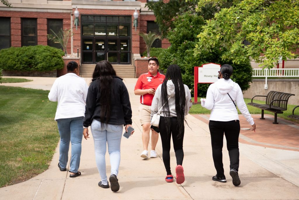 A Preview guide talks to a student and their family about what departments are located in each of the buildings during a tour of campus.