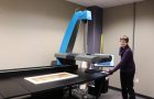 person stands in front of computer next to a large format scanner bed
