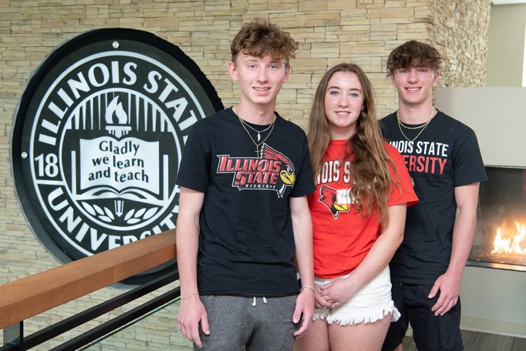 Three students stand in front of the Illinois State crest