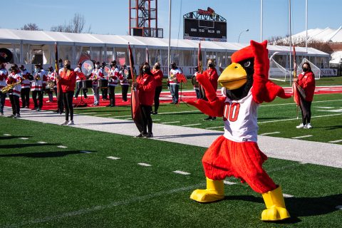 Reggie Redbird on the football field in front of color guard members