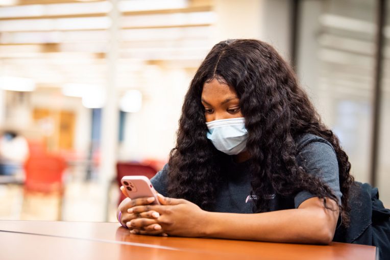 A masked student looks at her phone in Milner Library.