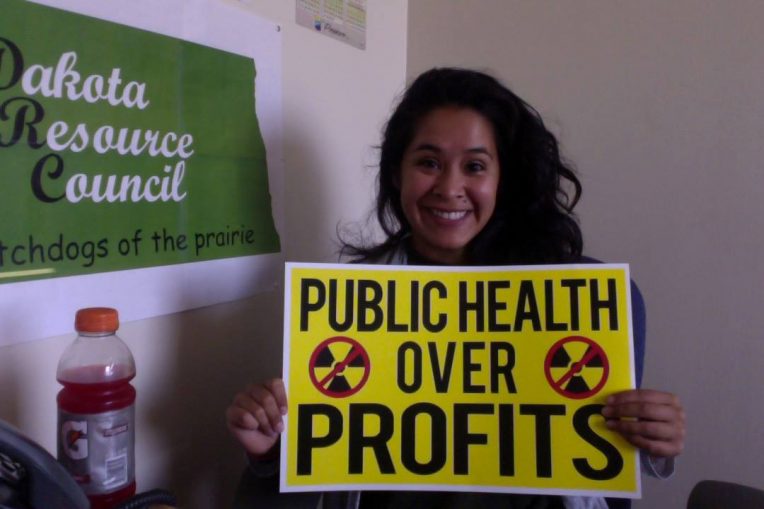 Stevenson Center alum Cecilia Montesdeoca holding up a small yellow sign that says "Public Health Over Profits"