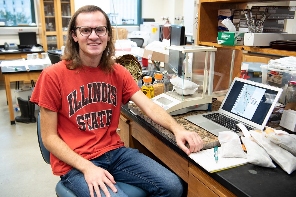 Portrait of Alex Hafner next to his research in a lab.