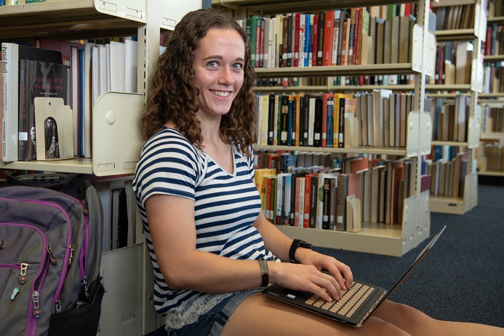 Portrait of Audrey Harrod in the library with her laptop.
