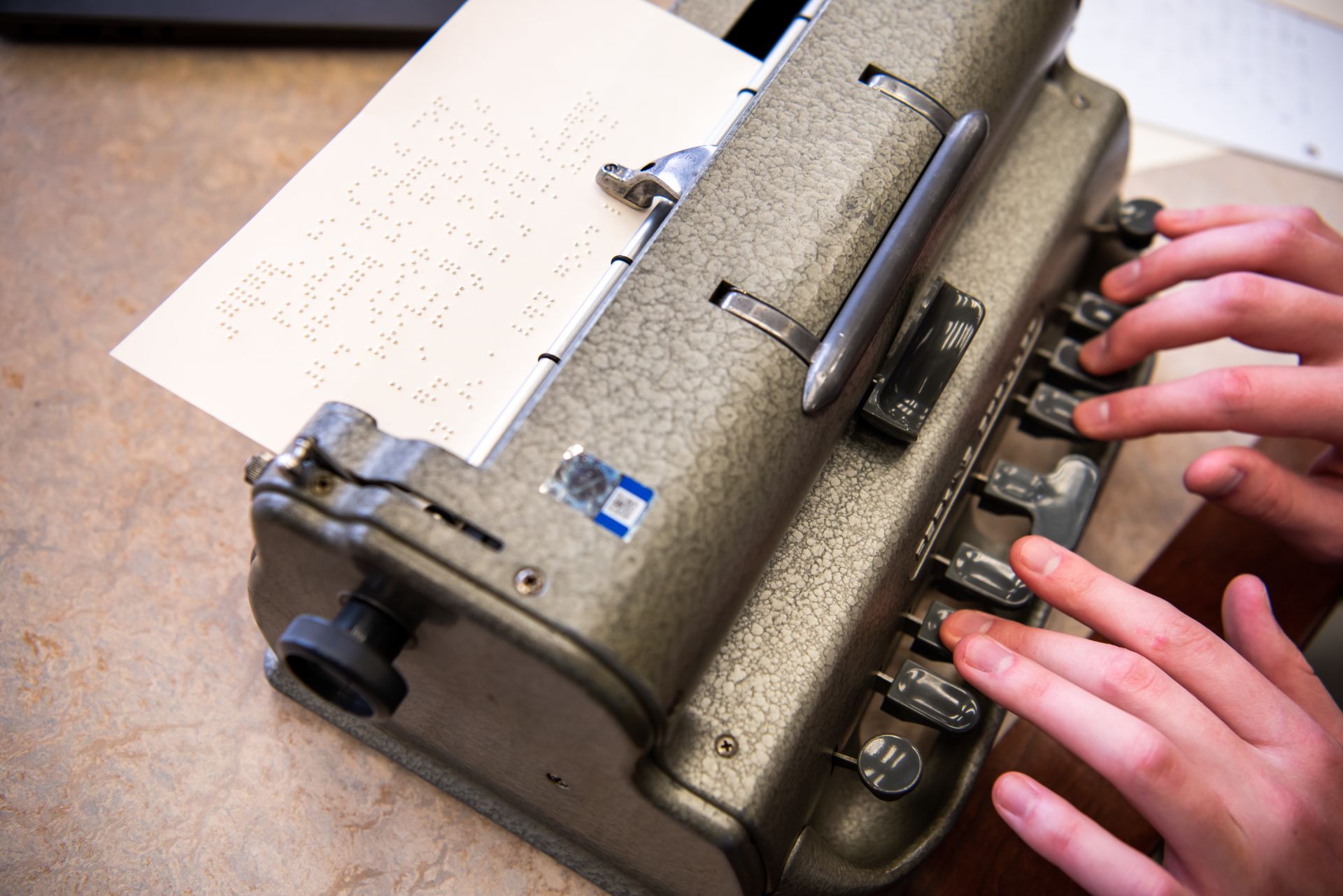 Close up shot of Martin's hands as she practices her braille with a brailler.