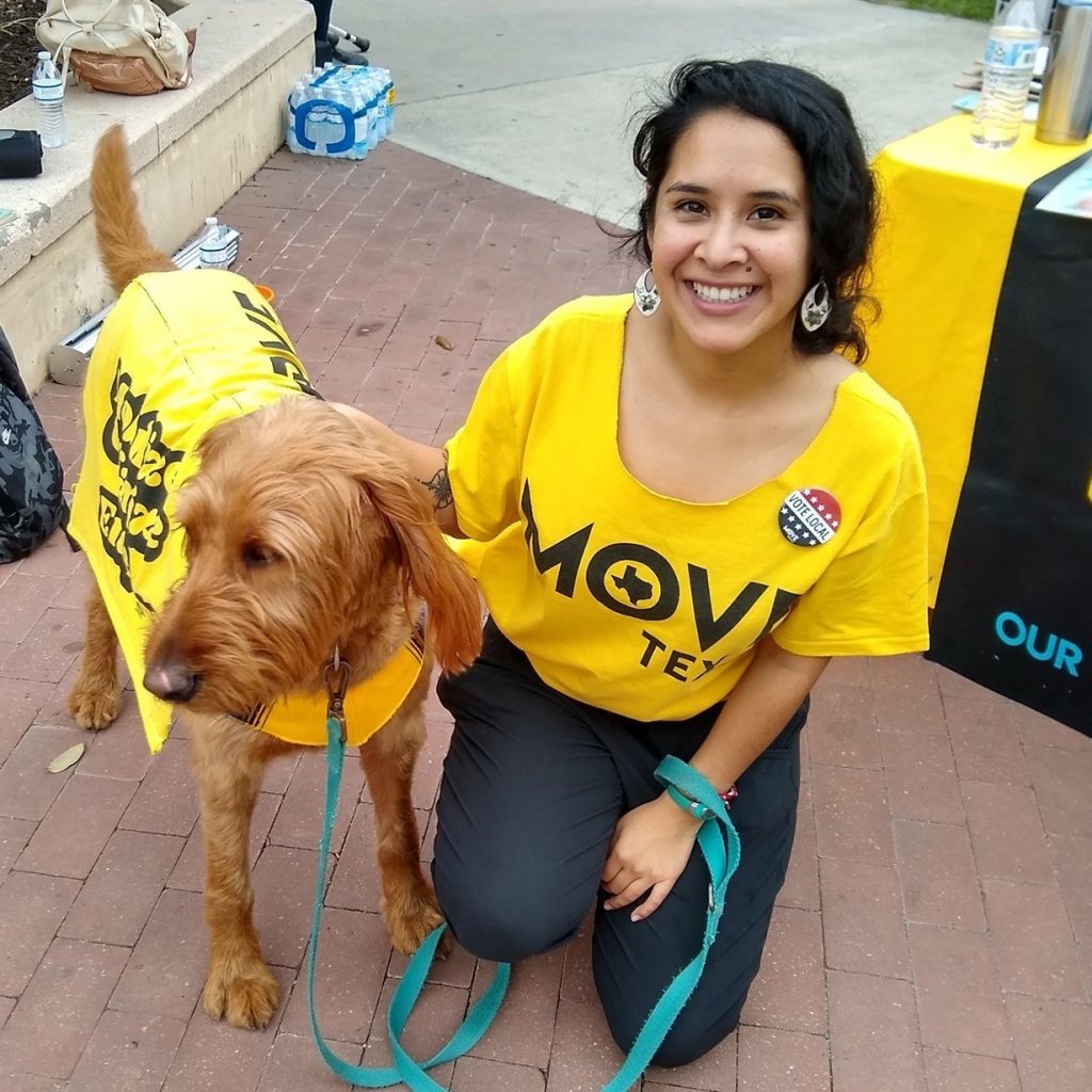 Cecilia Montesdeoca, a Stevenson Center alum, posing with a dog during a MOVE Texas event. Both are wearing MOVE Texas branded clothing.