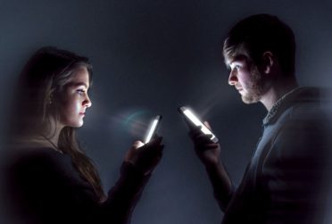 Illinois State magazine cover two people in a dark room facing each other but staring a their smartphones