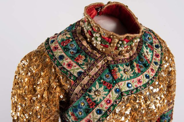 a photograph of the shoulders and neck area of a circus wardrobe piece adorned with gold sequins and a floral pattern around the top area