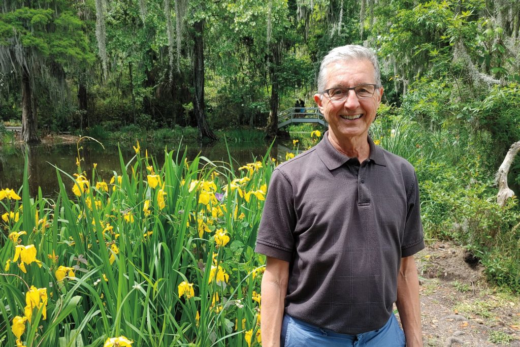 Portrait of David DeMarini smiling in front of a yellow flower garden.