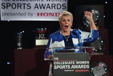 Chris Voelz stand behind a podium with her hand raised in a fist.
