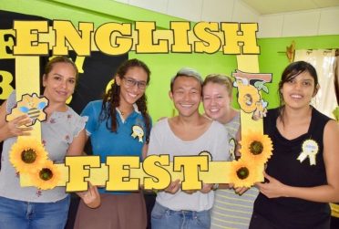 Five people holding up a yellow, hollow sign that says "English Fest" on it in a classroom