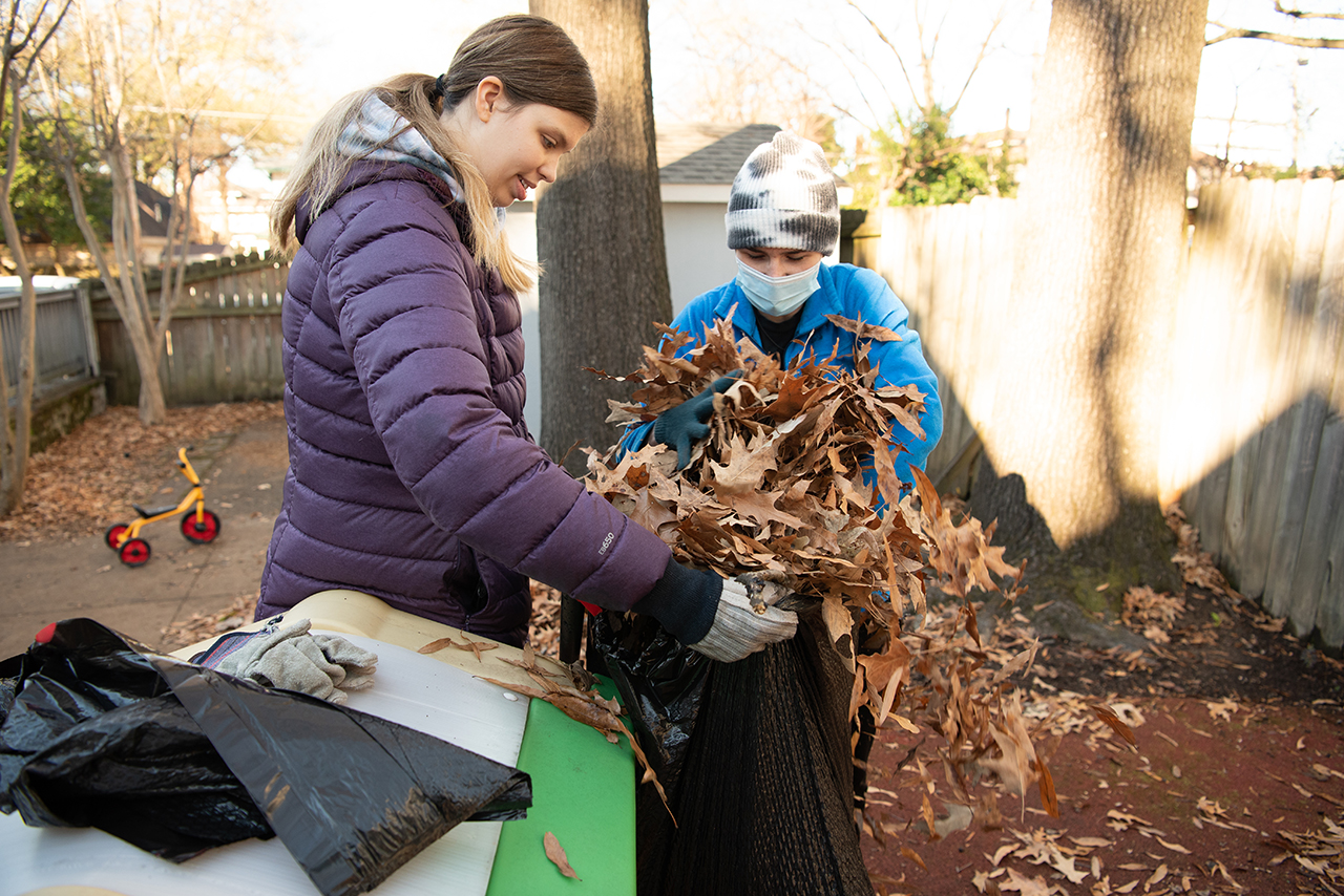 Junior Nicole Martin, left, holds a garbage bag open as senior Rylie Linn, right, fills the bag with leaves they raked up from the playground at Hope House.