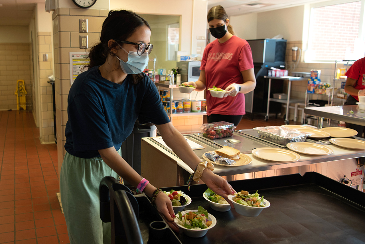First-year graduate student Joie Pecoraro, left, and junior Nicole Martin, right, place prepared salad on a tray before serving the first part of lunch to homeless people at Room In The Inn.