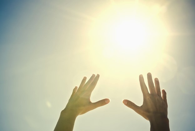 Hands reaching up towards the sky and sun