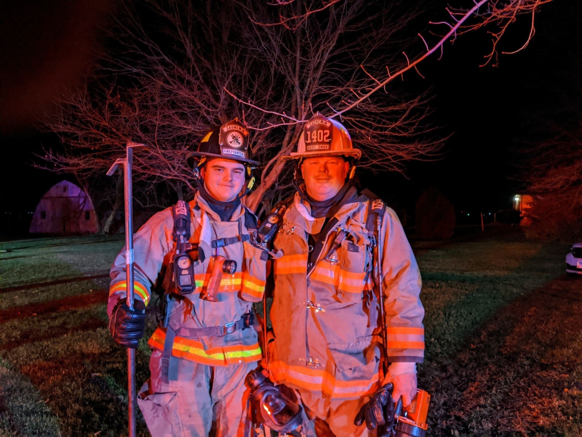 father and son firefighters pose in their protective gear.