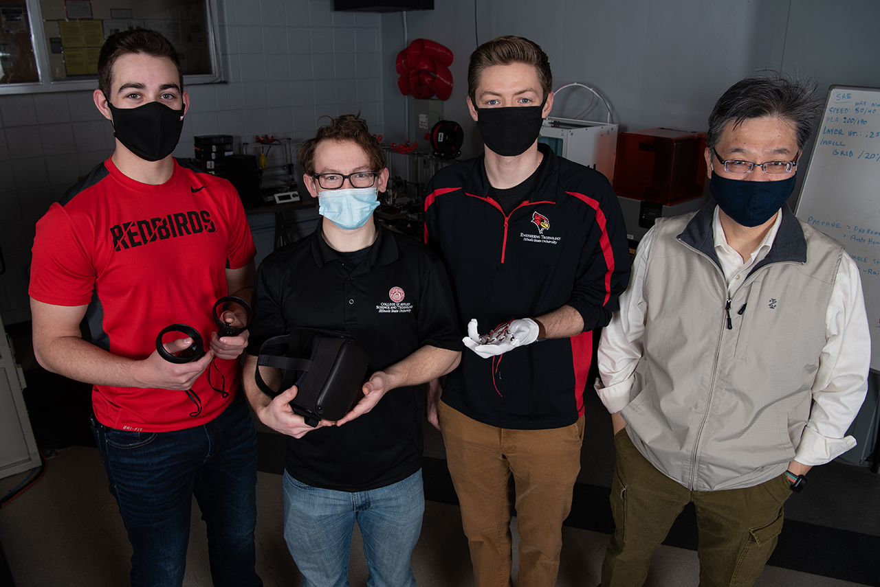 Jake Weihe stands on the far left holding a VR controller in each hand. Alex Diffor stands beside him holding a VR headset. To the right of him, Jordan Osborne stands holding out a hand wearing a white haptic glove. Dr. Isaac Chang stands next to him, on the far right.