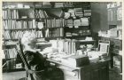 A black and white vintage photo of a woman sitting in a chair surrounded by books.