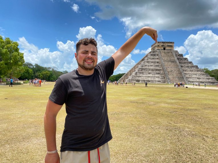 Student pointing at Mayan temple in an open field on a sunny day