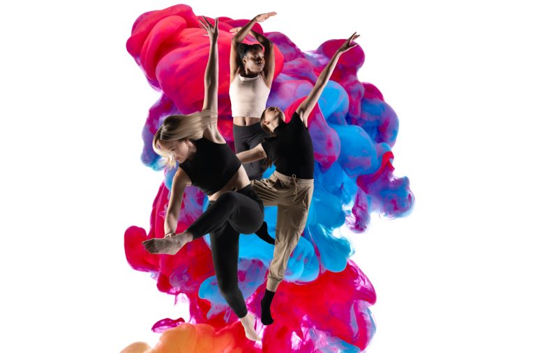 3 dancers in front of colorful smoke