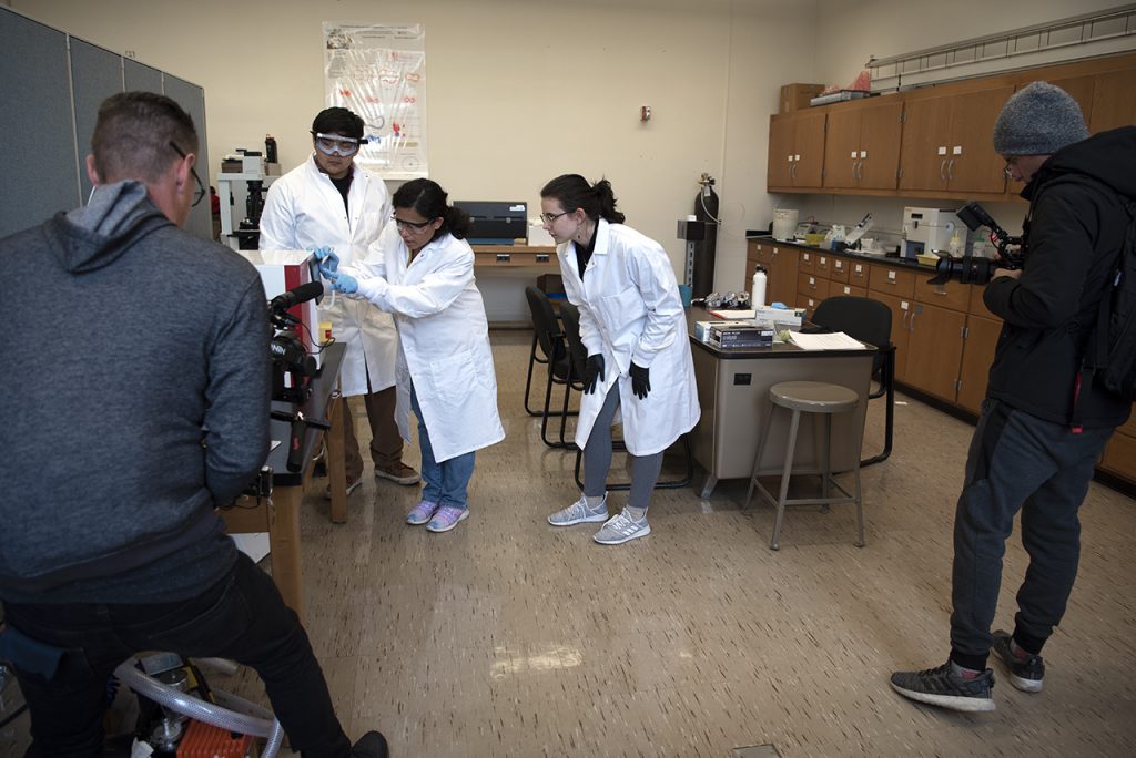 Students working in a lab and a faculty are depicted