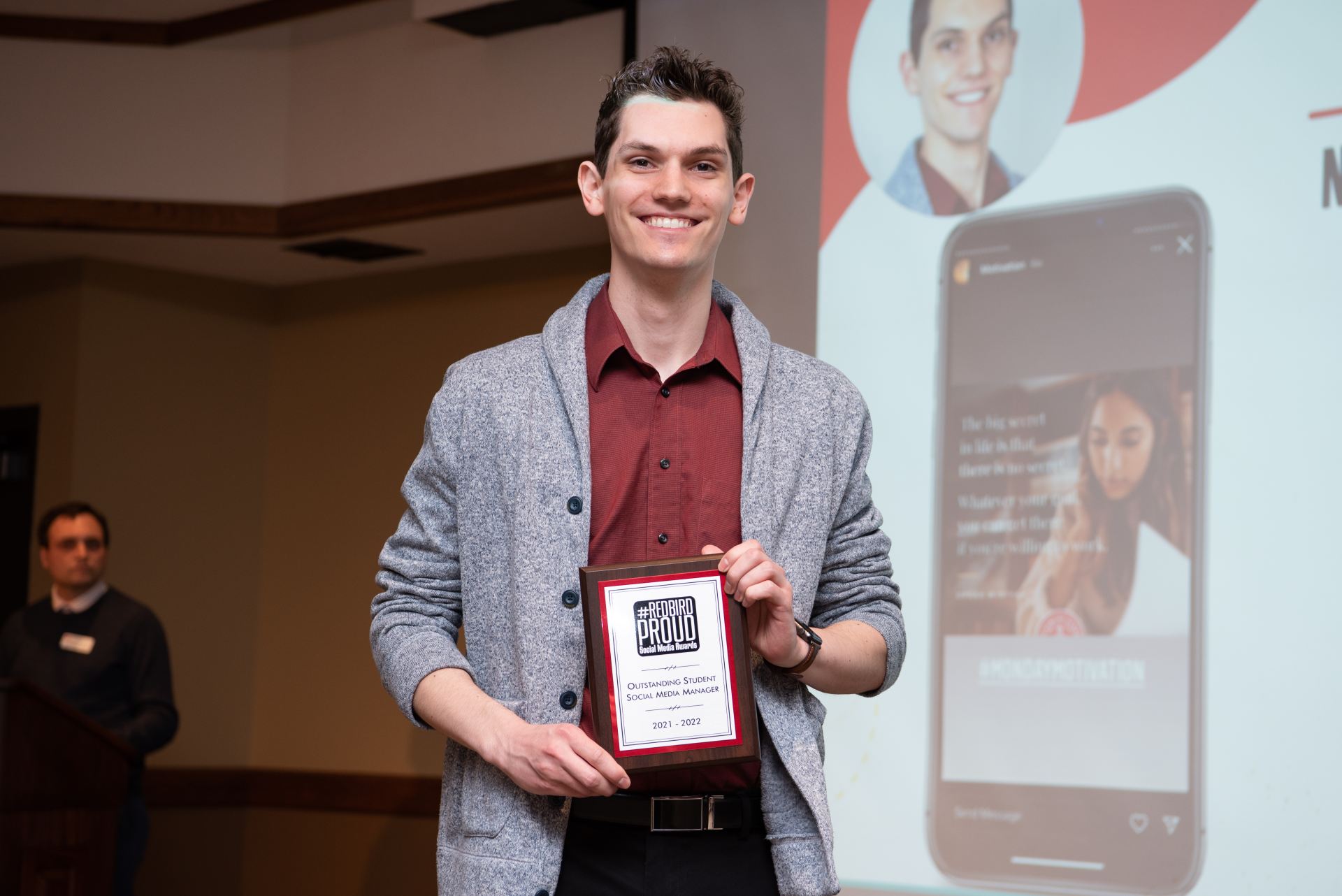Person posing while holding a plaque at an award ceremony.