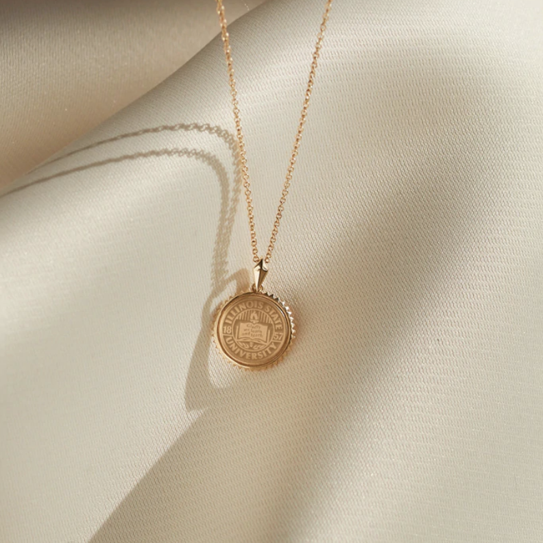 Gold ISU seal pendant necklace on an ivory silk background