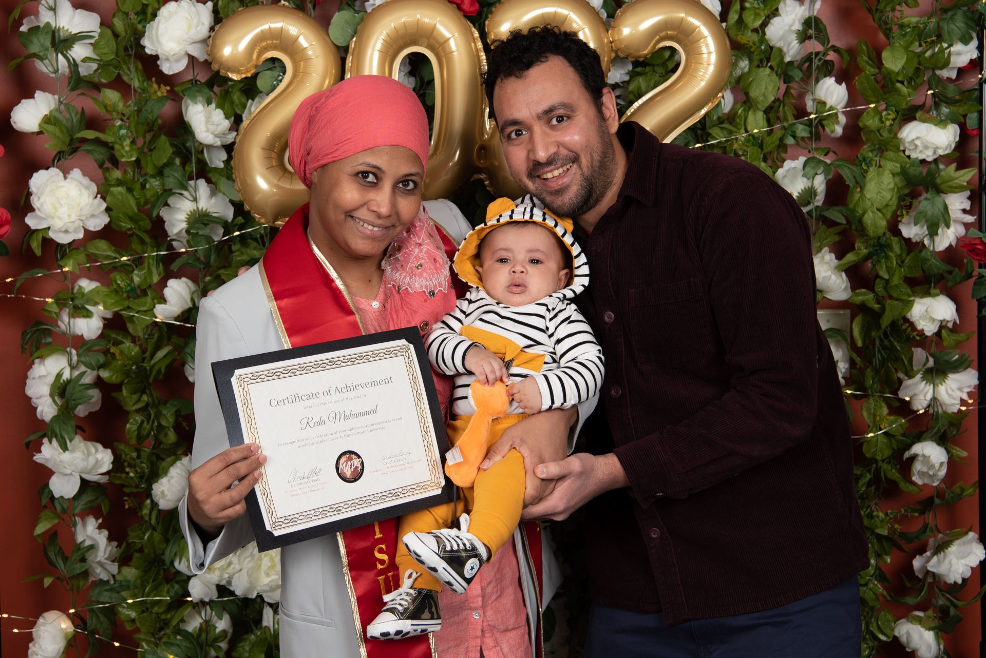 A student graduate posing with a baby and another person.