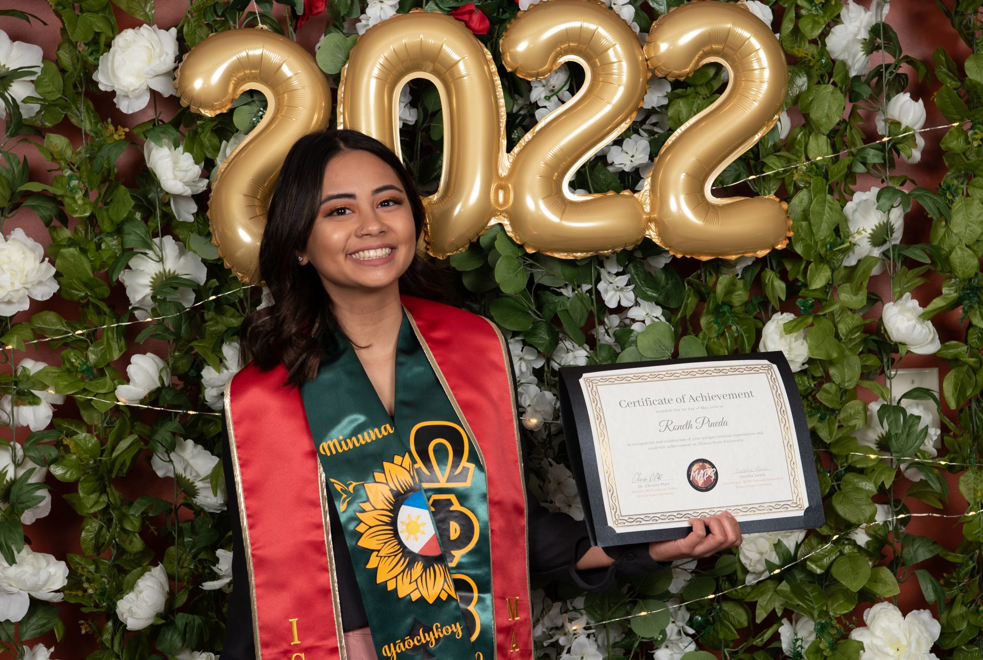 A graduate posing while holding their diploma.