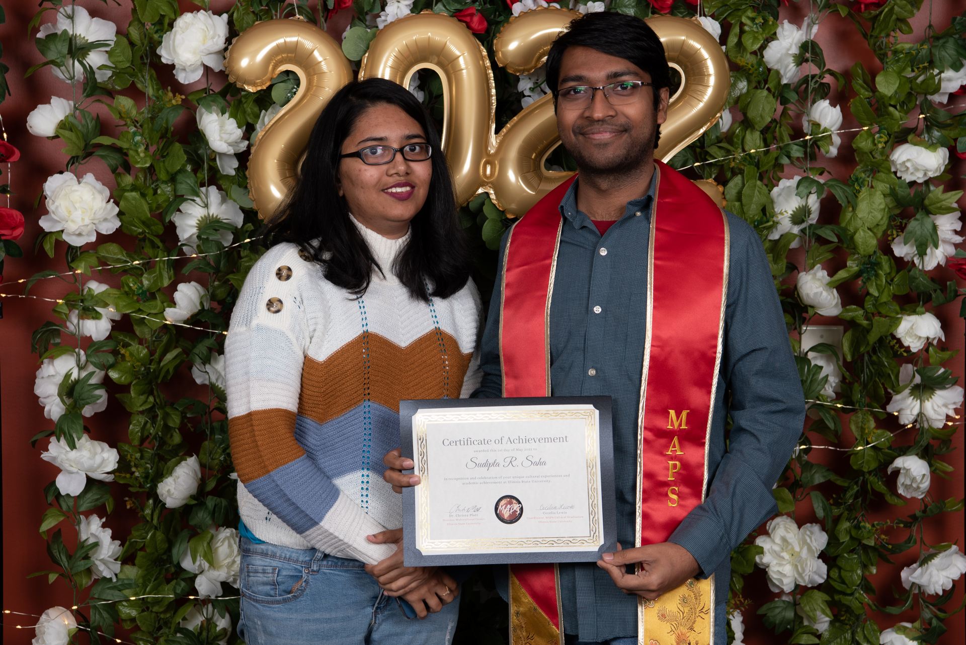 Two people standing side by side together as one person holds their diploma.