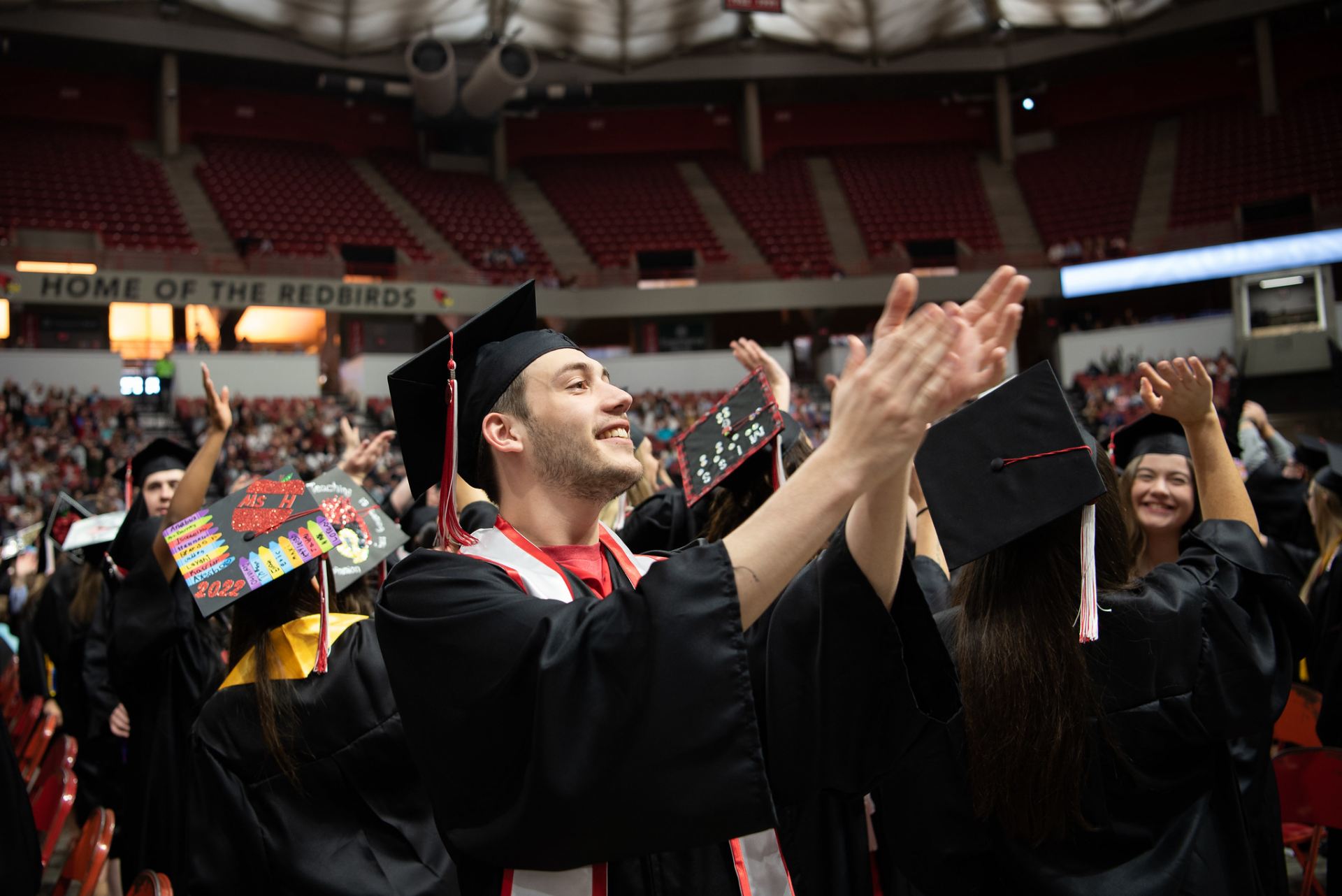 A person clapping their hands in the air as other graduates are in the background.
