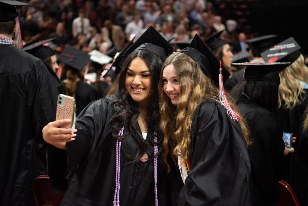 Two graduates take a selfie on a phone.